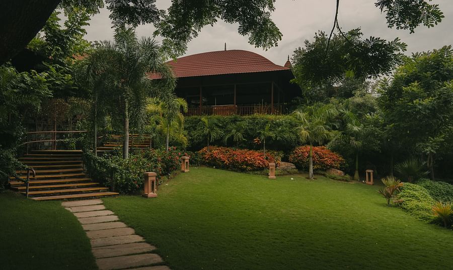 A scenic view of a building with a roof, surrounded by lush vegetation. A pathway leads to the building, suggesting a peaceful, natural setting.