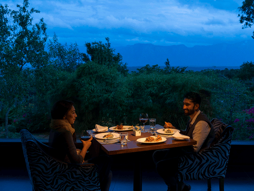 A couple enjoying a romantic meal outdoors in the evening with candlelight at The Serai Bandipur.