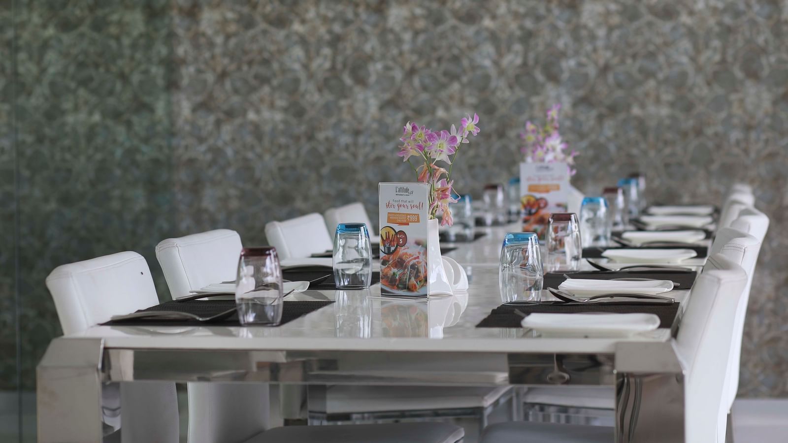 A long dining table set with white chairs, place settings, and colorful floral decorations | Restaurant | Grand Bay Resort and Spa