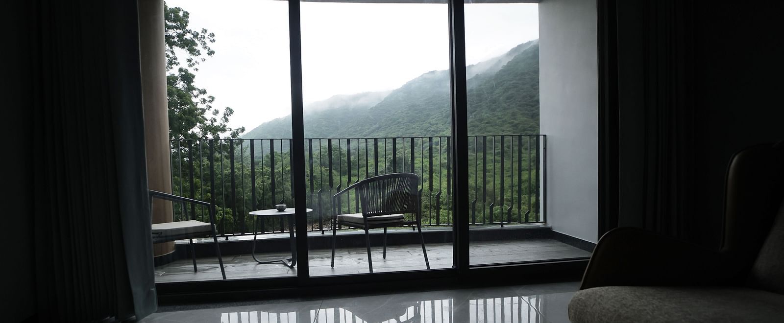 Club Suite with Valley View Sitout with sliding glass doors leading to a balcony overlooking a mountainous landscape at The Qualia Resort Club & Brewery, Udaipur.