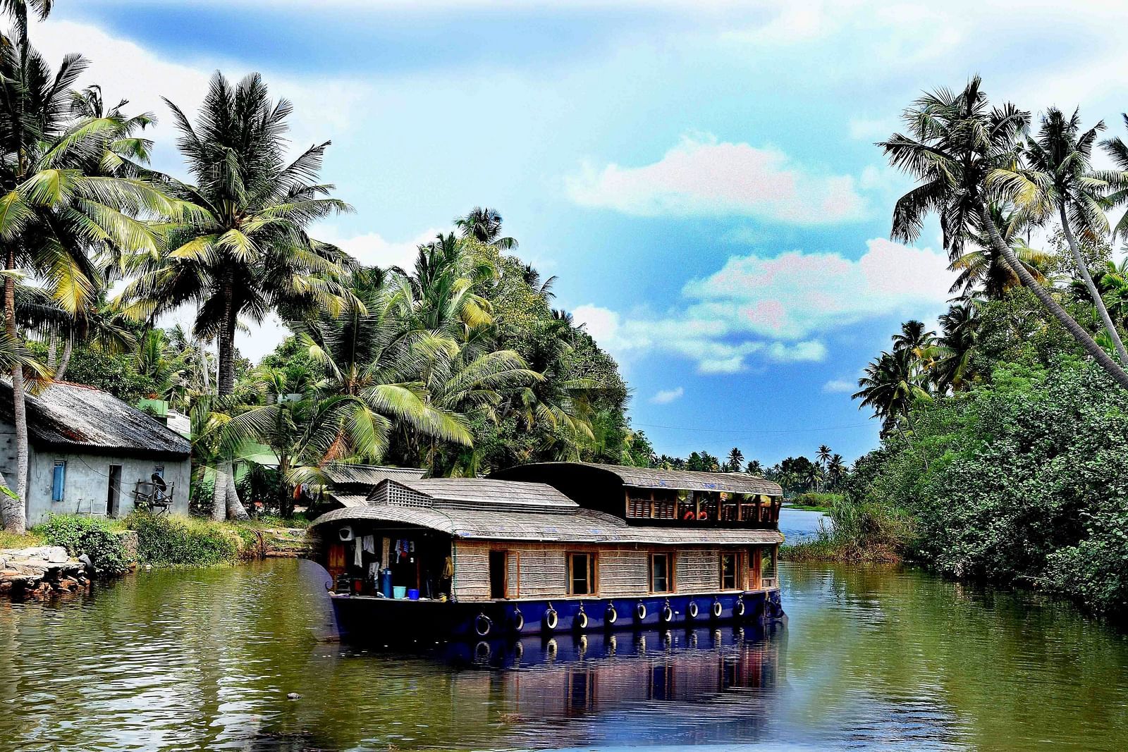 A houseboat in the kumarakom backwaters with coconut tress on both the side.