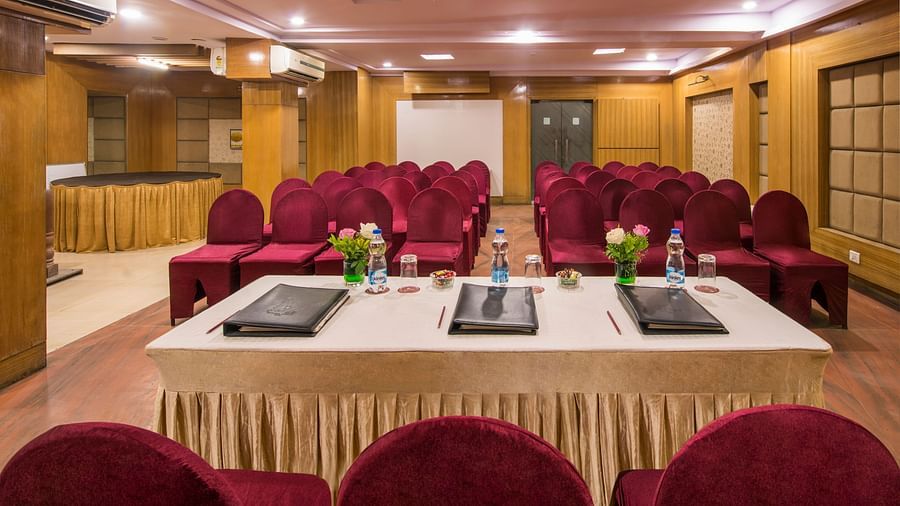 A smaller meeting room with a white table, laptops, and red cushioned chairs - Lords Eco Inn Dahej