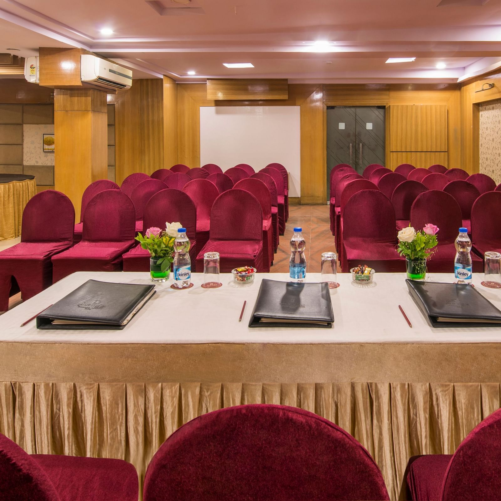 A smaller meeting room with a white table, laptops, and red cushioned chairs - Lords Eco Inn Dahej