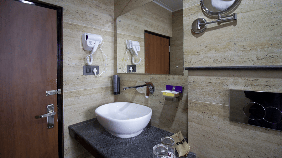 A bathroom featuring a basin vanity, a wall mounted hair dryer, a mirror, and tiled walls at Valmere Lungta Boutique Hotel & Spa, Darjeeling.