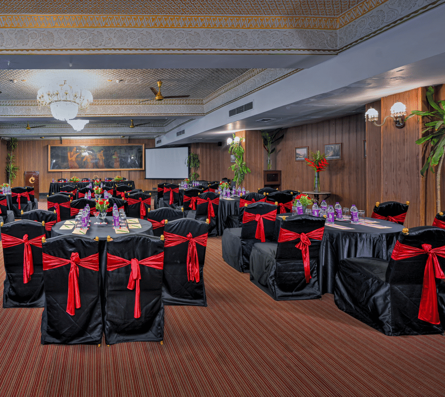 A hall at The Clarks Varanasi, with chairs, tables, and a chandelier.