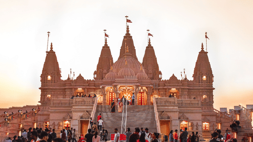 Front view of the BAPS shri Swaminarayan mandir with devotees surrounding it during sunset.