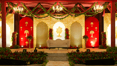 A decorated stage with a red backdrop and floral arrangements, likely set up for a wedding reception or event.