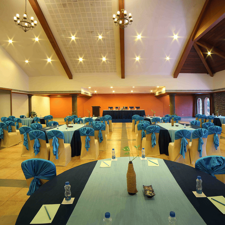 A spacious venue of Vizhinjam Hall at Uday Samudra Leisure Beach Hotel, Kovalam, set up for an event with round tables and blue-covered chairs.