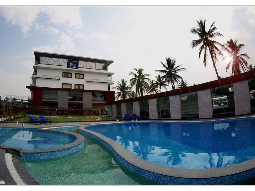 image of a beautiful swimming pool with clear waters surrounded by green trees situated in front of the resort building - Royal Lotus View Resotel