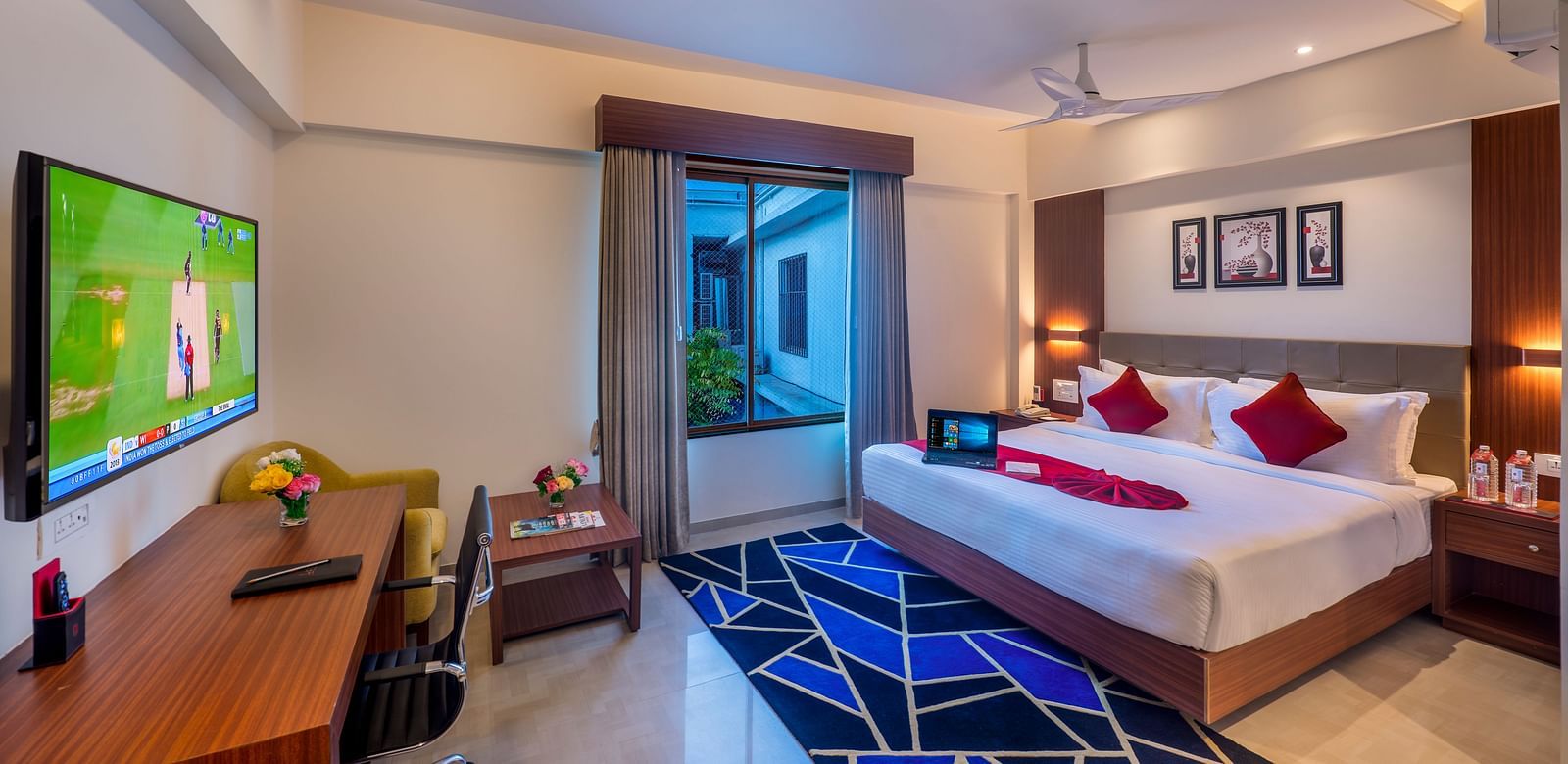 A hotel room with a bed featuring blue and white bedding, a television, and a view of the outside.