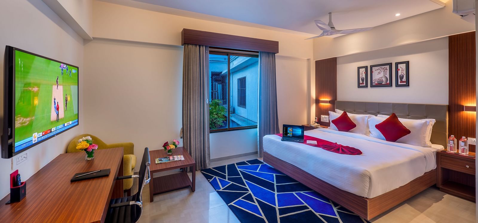 A hotel room with a bed featuring blue and white bedding, a television, and a view of the outside.