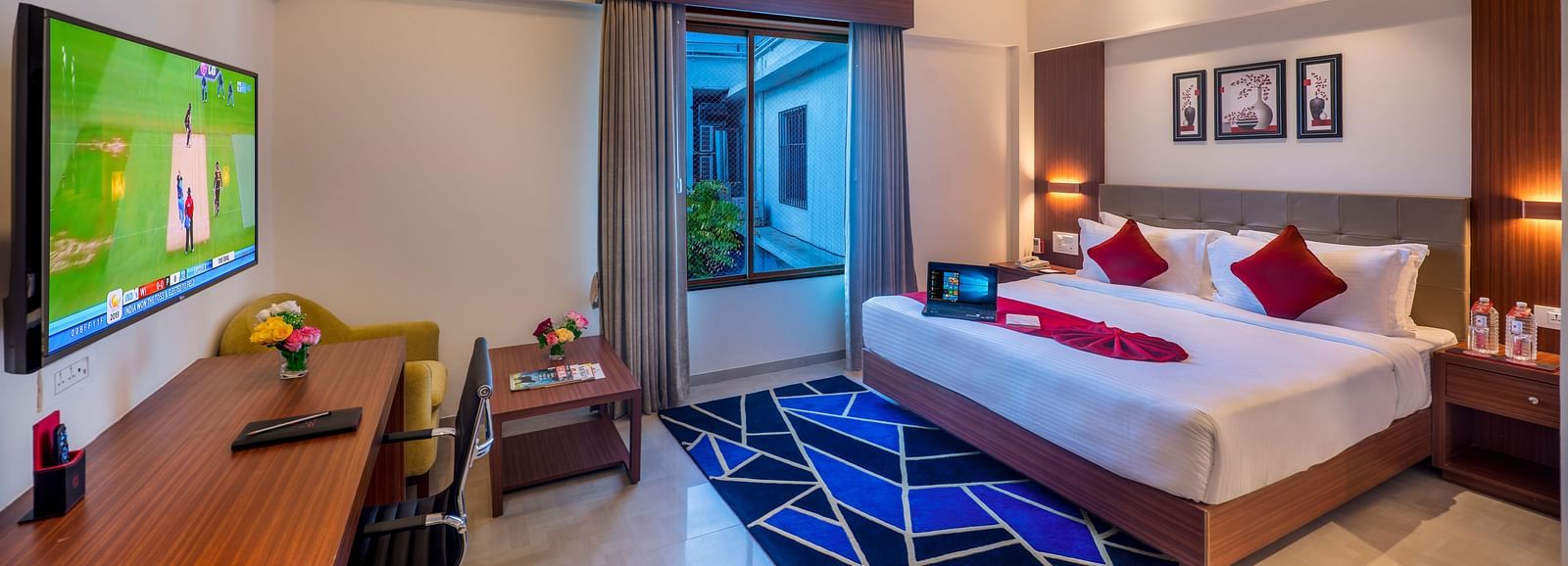 A hotel room with a bed featuring blue and white bedding, a television, and a view of the outside.
