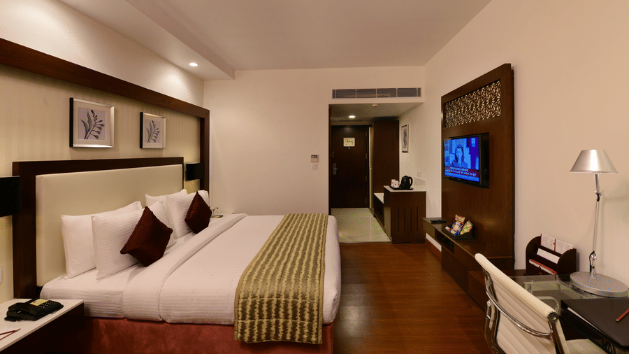 A double bed room with TV, side table, work desk and hallway to bathroom
