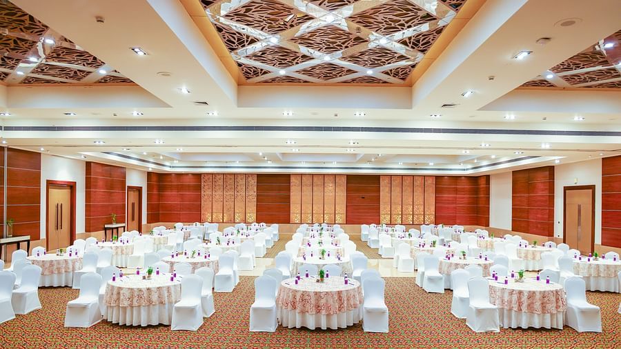 Event hall setup with round tables, white chair covers, and vibrant floral centrepieces, designed for a sophisticated gathering - Balaji Sarovar Premiere, Solapur