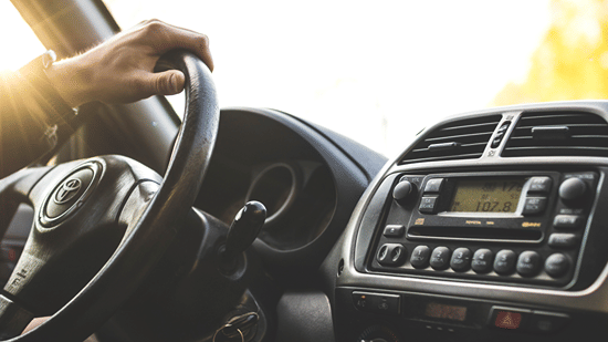 Close-up of a hand on a car steering wheel while driving.