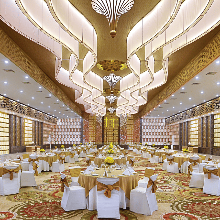 Banquet hall at The Bristol Hotel, Gurgaon set with round tables in gold runners, white chair covers with gold sashes, and yellow flower centrepieces.