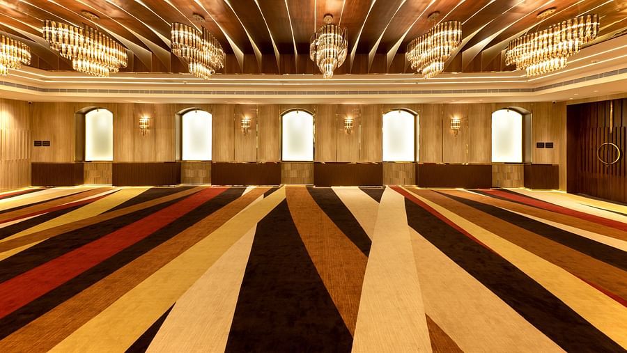 Striped carpeted hall with arched frosted windows, gold chandeliers and curved wooden ceiling panels at Jenneys Residency, Coimbatore