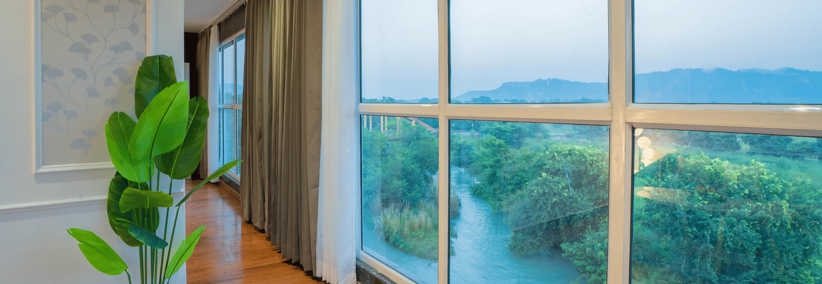 A hallway at Sukoon by the Ganges features floor-to-ceiling windows offering a tranquil view of the river and green landscape.
