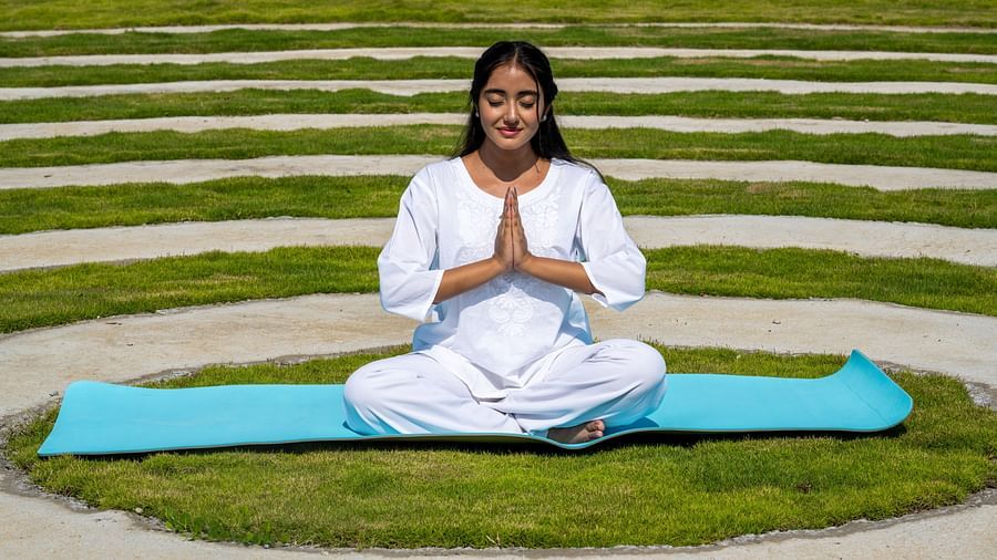 A close up shot of a woman dressed in white performing a yoga asan on a blue mat - Rajbagh Wellness, Udaipur