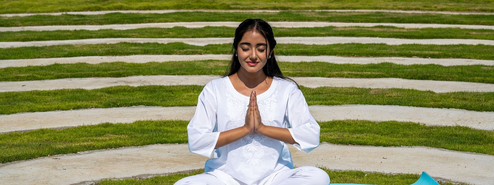 A close up shot of a woman dressed in white performing a yoga asan on a blue mat - Rajbagh Wellness, Udaipur