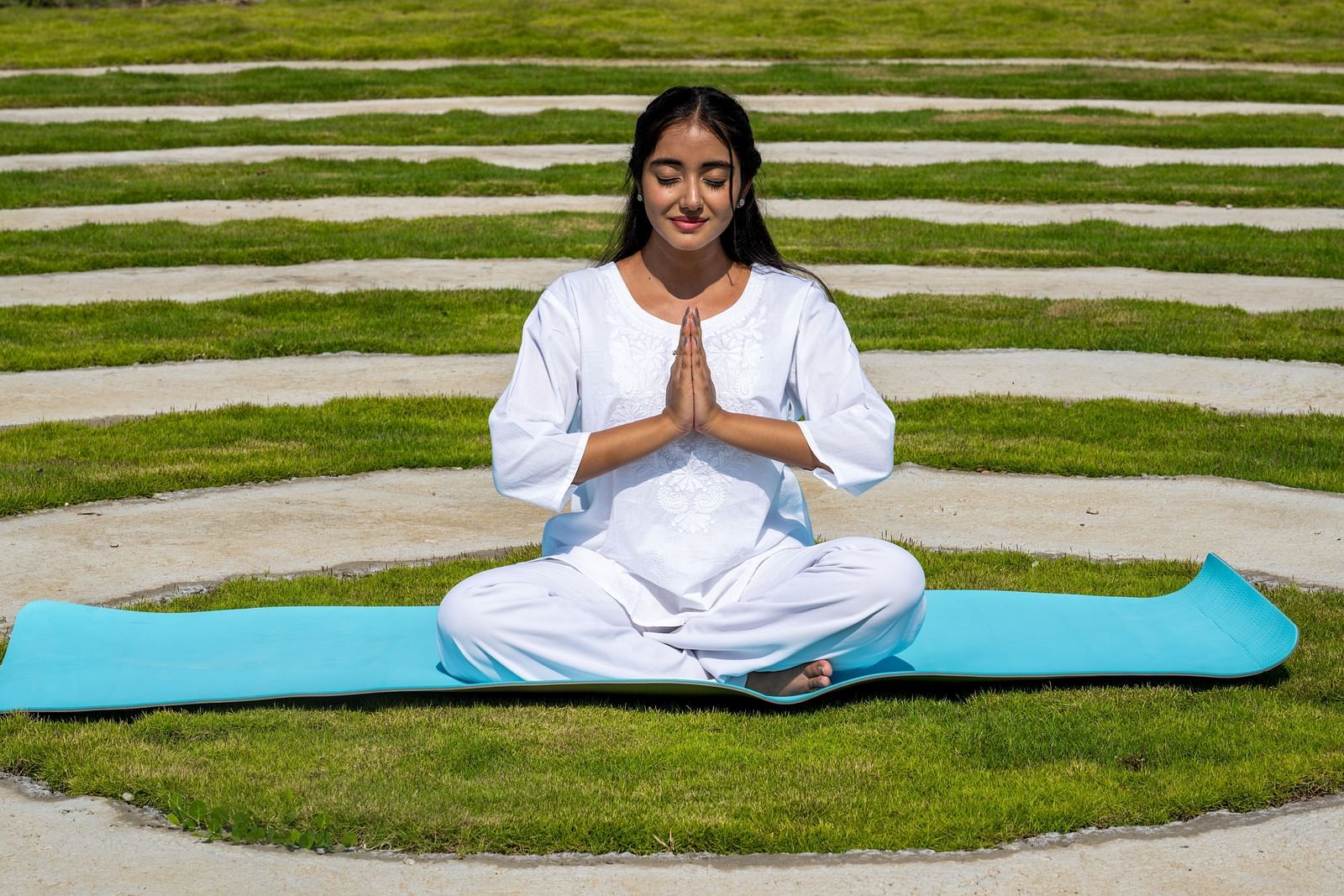 A close up shot of a woman dressed in white performing a yoga asan on a blue mat - Rajbagh Wellness, Udaipur