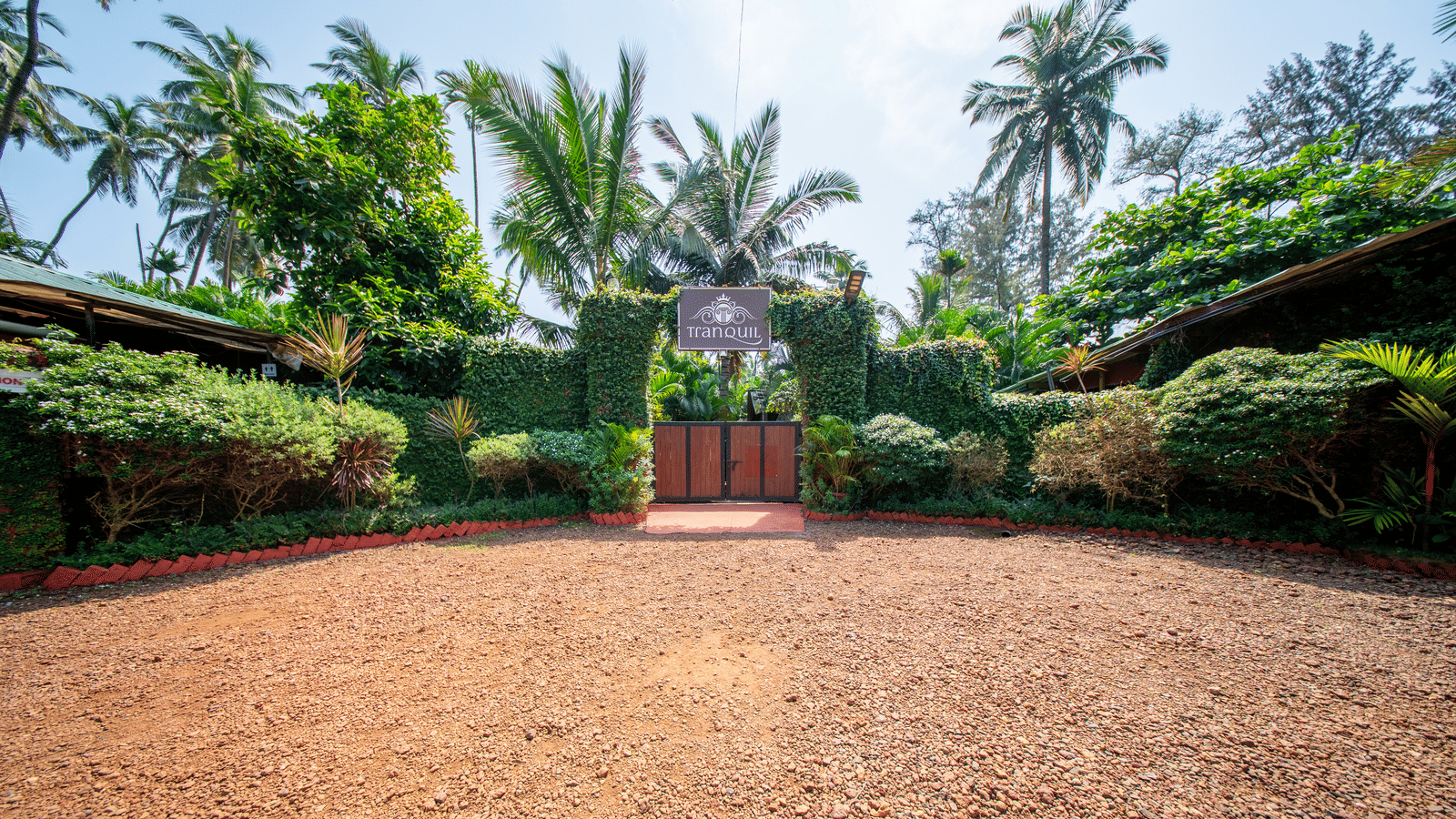 Garden with pathway, bushes, palm trees, small entrance gate at Tranquil Group.