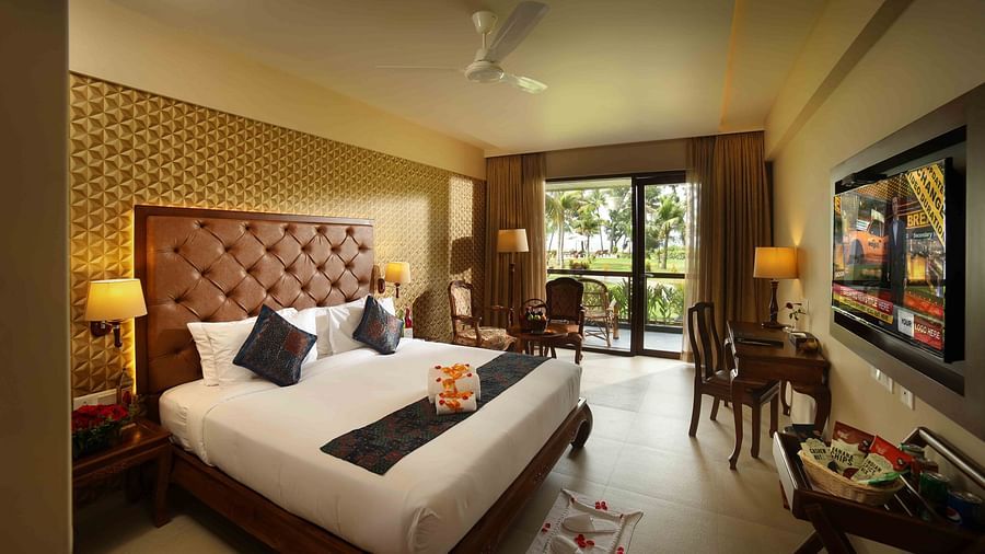 Lake view Deluxe Room at Uday Backwater Resort featuring a plush bed facing the TV mounted on the wall and a work desk next to the TV behind which is a cosy sitting space by the window