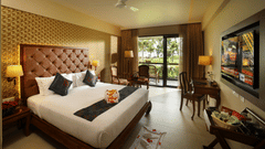 Lake View Deluxe Room at Uday Backwater Resort features a plush bed facing a wall-mounted TV, with a work desk beside it and a cosy seating nook by the window behind