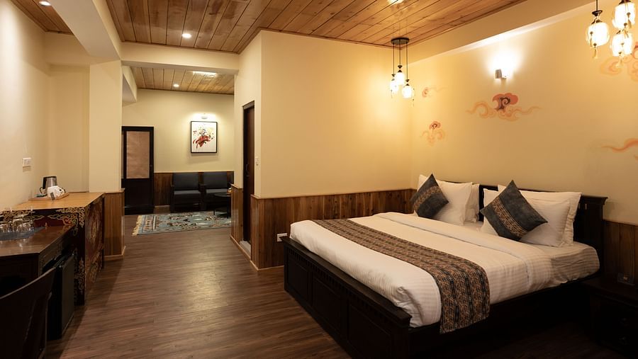 A full view of a well-lit room that has a bed and wooden tables | Voyage The Royal Retreat, Gangtok