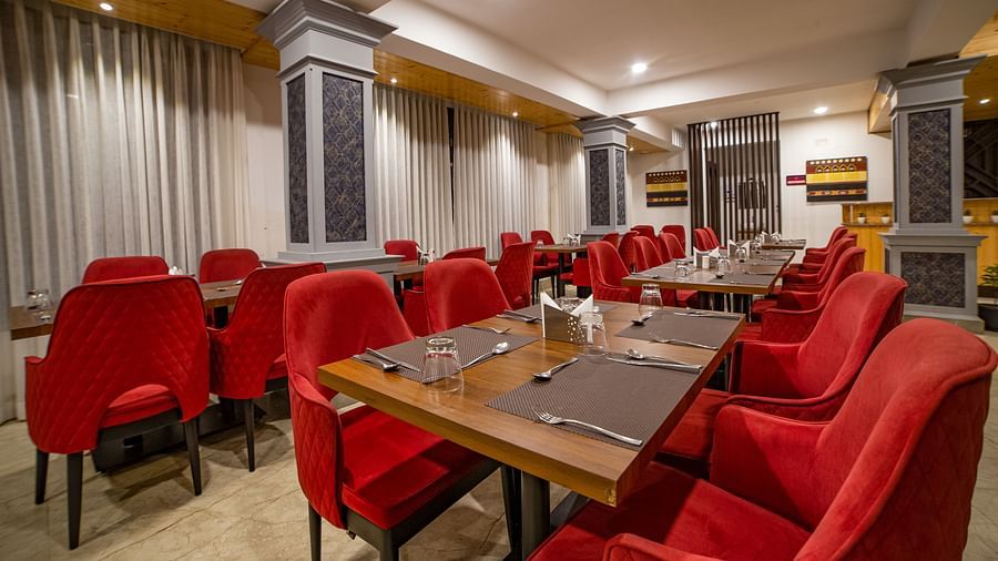 Dining area  in Sumitel Hotel with multiple red-cushioned chairs and tables, stylish lighting, and patterned wall panels.
