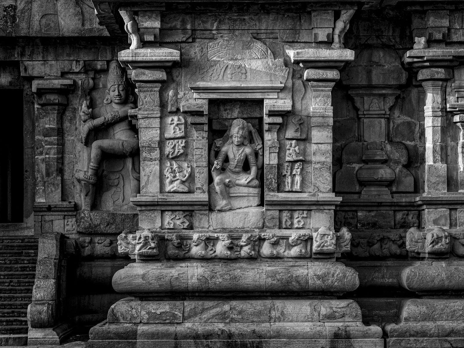 Grayscale close-up of a section of an ancient temple wall, adorned with detailed stone carvings of deities and figures.