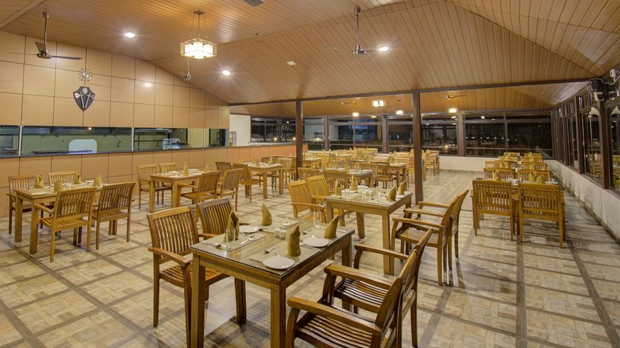 A spacious dining area with comfortable chairs around tables under a warmly-lit ambience | Sheesham Restaurant | Woodstock Resorts, Coorg