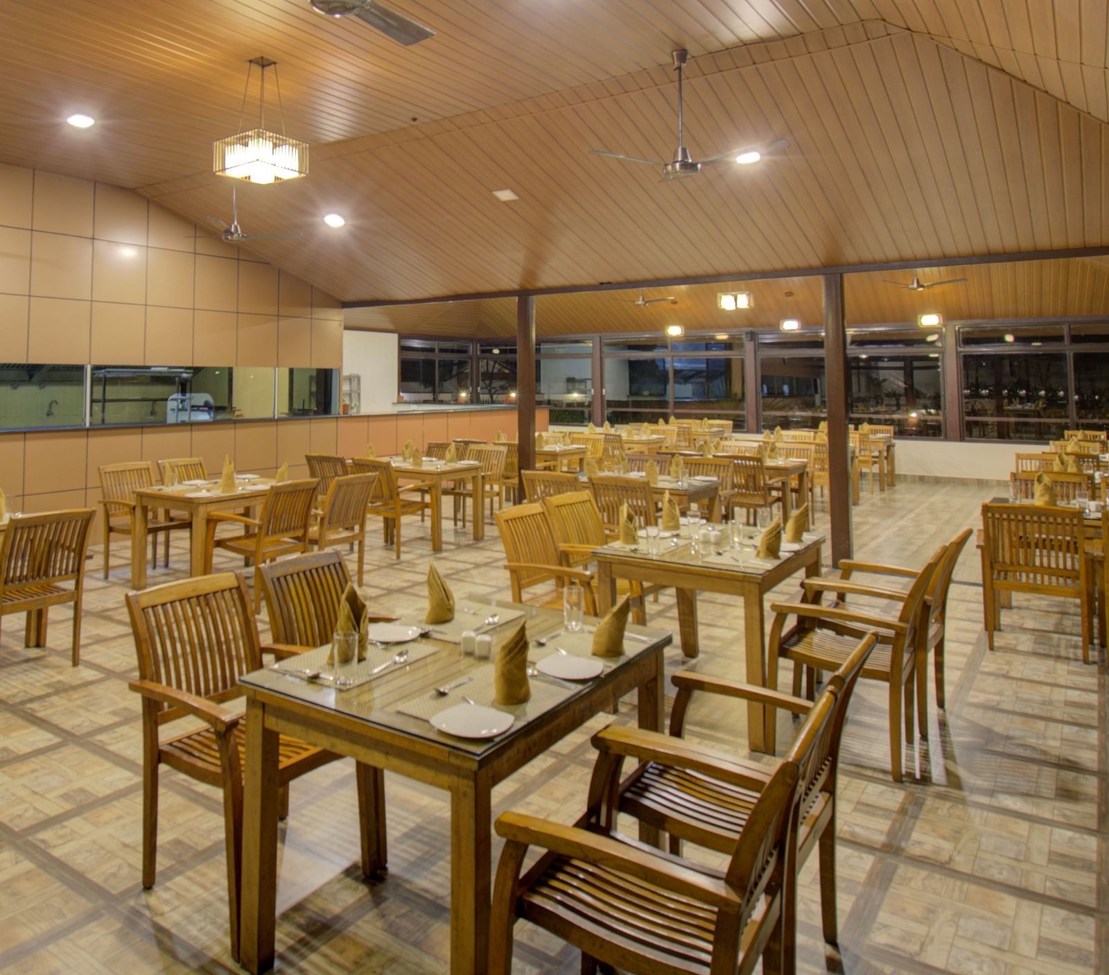 A spacious dining area with comfortable chairs around tables under a warmly-lit ambience | Sheesham Restaurant | Woodstock Resorts, Coorg
