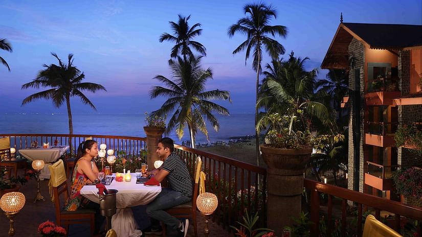 A couple enjoying candlelight dinner at Uday Samudra Leisure Beach Hotel amid ambient lighting with a backdrop of evening sky with different hues of blue