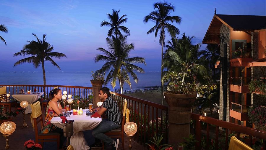 A couple enjoying candlelight dinner at Uday Samudra Leisure Beach Hotel amid ambient lighting with a backdrop of evening sky with different hues of blue
