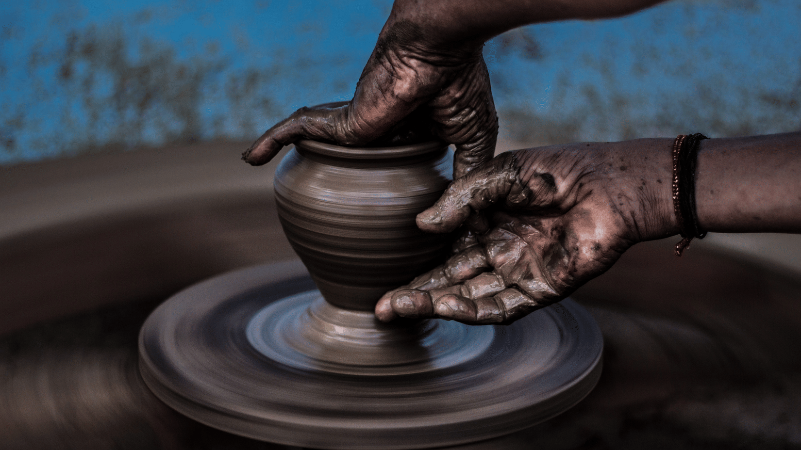 A potter’s hands covered in clay, shaping a small pot on a spinning wheel