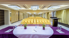 View from a speaker's table with purple cloth towards a large conference room filled with rows of yellow chairs at Golden Tulip Kukas, Jaipur.