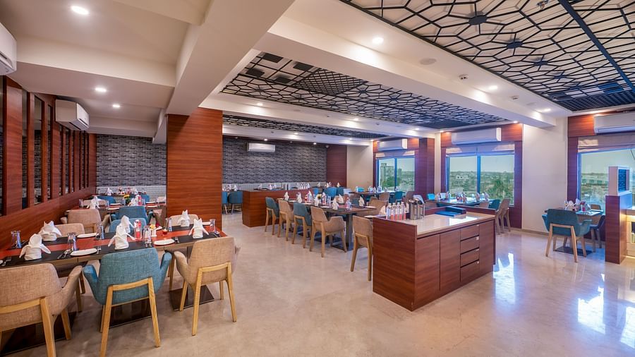 Spacious restaurant with neatly arranged tables and comfortable seating - Lords Eco Inn Shapar Rajkot