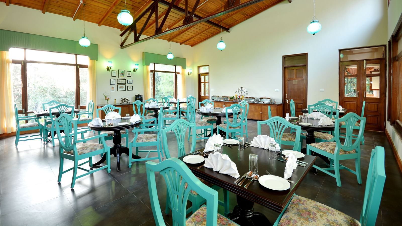 An image of a cafe in Almora with teal coloured chairs, black tables and ambient lighting - BluSalzz Escapade - Anant Rasa Resort