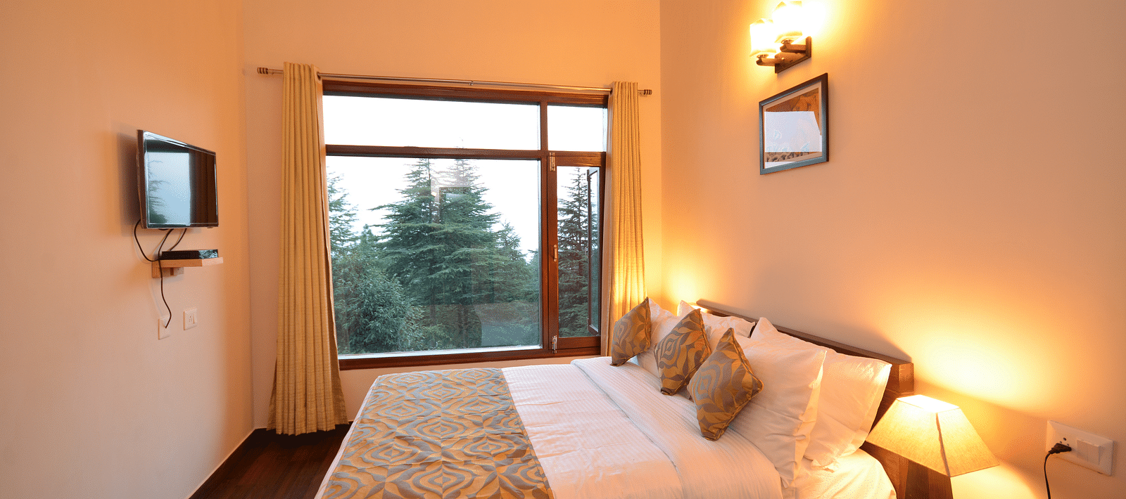 A bedroom with warm lighting, a comfortable bed, and a window overlooking lush greenery - BluSalzz Escapade - Anant Rasa Resort