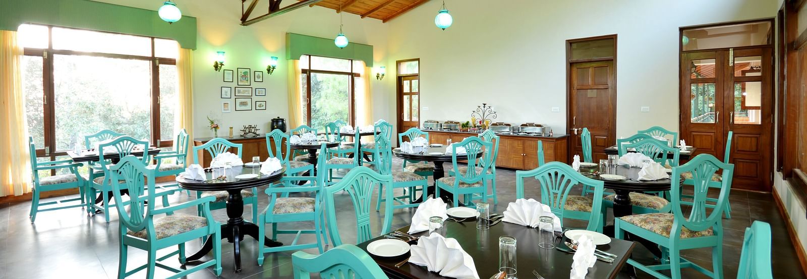 An image of a cafe in Almora with teal coloured chairs, black tables and ambient lighting - BluSalzz Escapade - Anant Rasa Resort