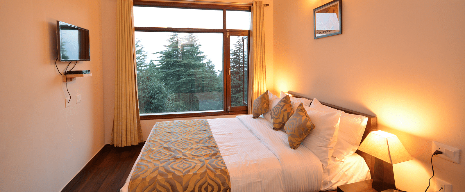 A bedroom with warm lighting, a comfortable bed, and a window overlooking lush greenery - BluSalzz Escapade - Anant Rasa Resort