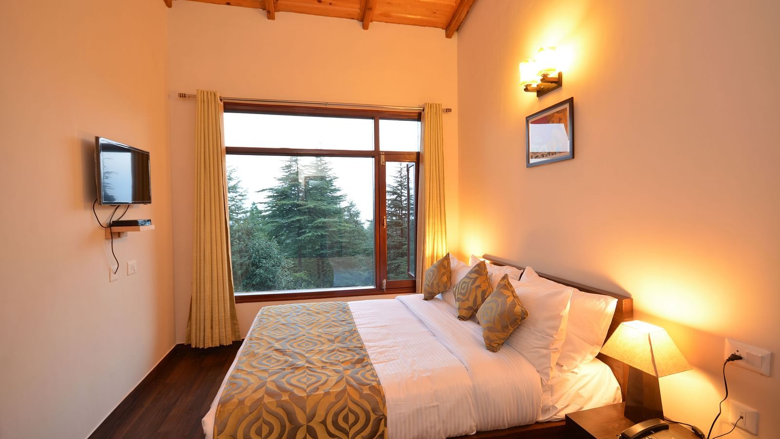 A bedroom with warm lighting, a comfortable bed, and a window overlooking lush greenery - BluSalzz Escapade - Anant Rasa Resort