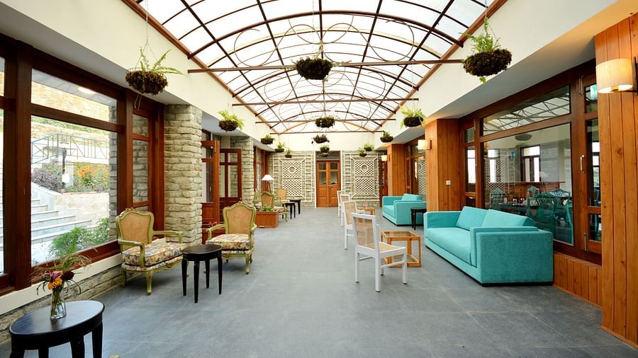 A well-lit lounge area with teal coloured sofas, cosy chairs, teapoys, and plants hung from the ceiling - BluSalzz Escapade - Anant Rasa Resort