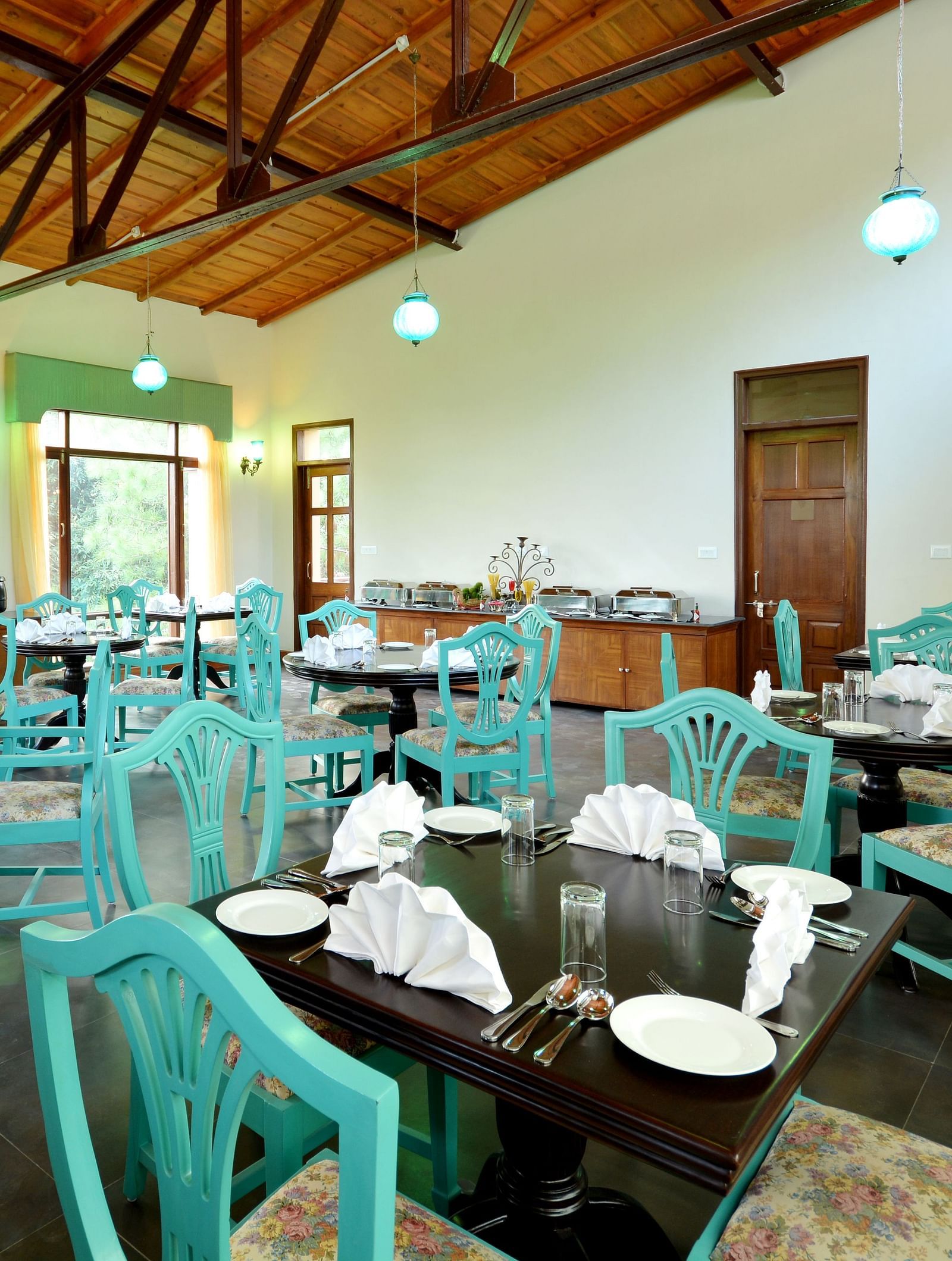 An image of a cafe in Almora with teal coloured chairs, black tables and ambient lighting - BluSalzz Escapade - Anant Rasa Resort