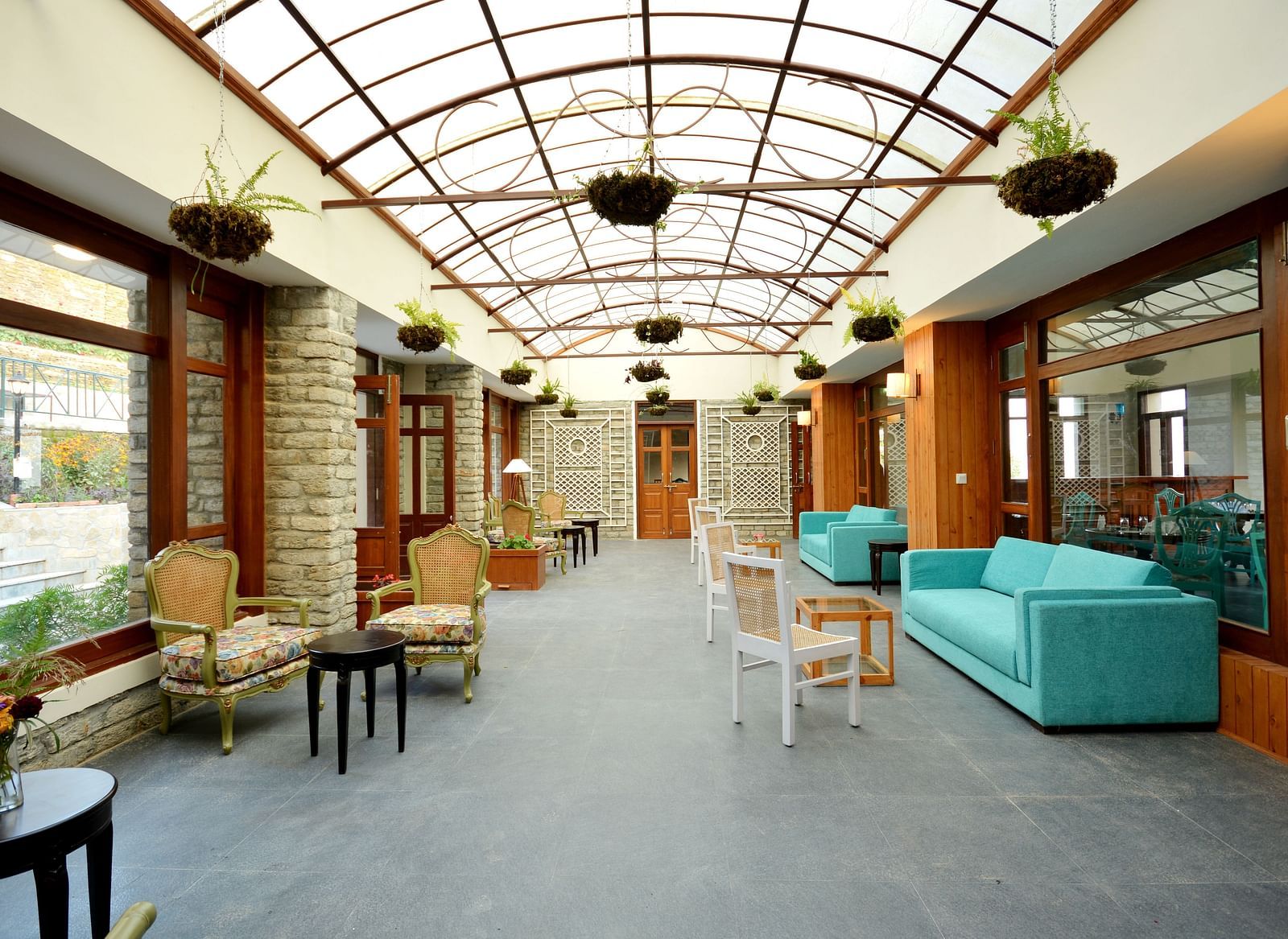 A well-lit lounge area with teal coloured sofas, cosy chairs, teapoys, and plants hung from the ceiling - BluSalzz Escapade - Anant Rasa Resort
