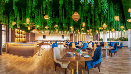 Vibrant restaurant at Lords Inn Sangam, Bhopal featuring blue and wooden chairs, dining tables, and a striking green hanging ceiling installation.