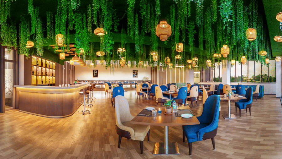 Vibrant restaurant at Lords Inn Sangam, Bhopal featuring blue and wooden chairs, dining tables, and a striking green hanging ceiling installation.