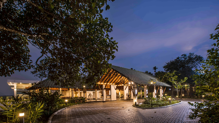 The resort entrance glowing at dusk with a curved driveway and warm ambient lights | Great Trails Wayanad by GRT Hotels