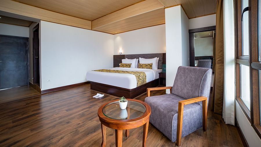 A sitting area  in Sumitel Hotel with two chairs and a round table, large windows letting in natural light, and wooden ceiling accents.